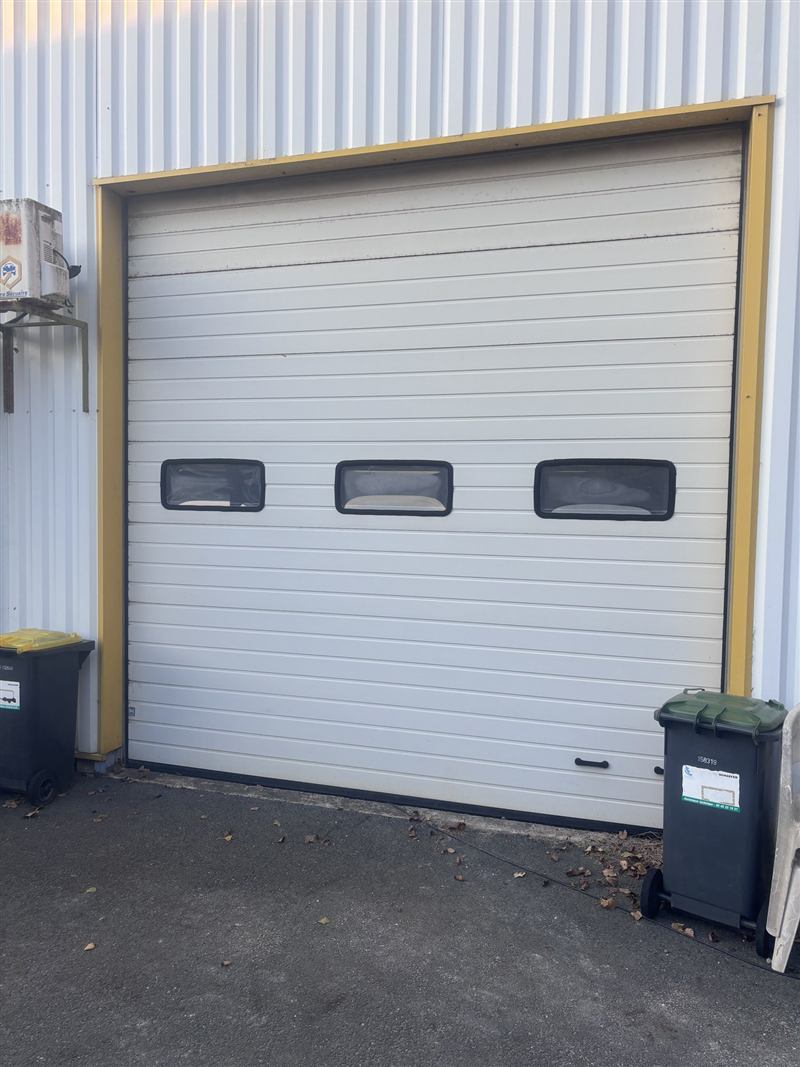 Porte de garage sectionnelle blanche à trois hublots, dans un encadrement jaune